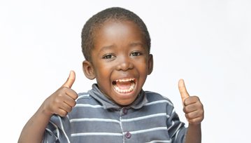 Child smiling while giving two thumbs-up