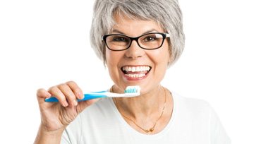 Smiling woman brushing her dental implants in Ann Arbor