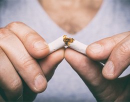 Closeup of smoker with dental implants in Ann Arbor breaking cigarette 