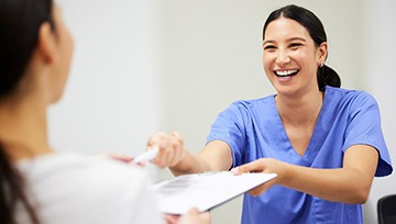 Dental assistant smiling while handing patient form