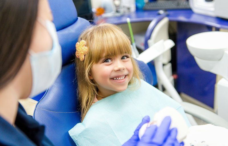 a little girl with a flower clip in her hair smiles at her dentist during a visit